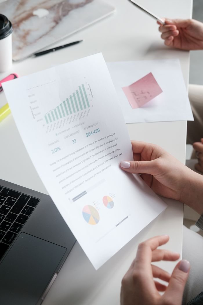 Offerings Hands holding a business report with graphs, in a modern office setting.